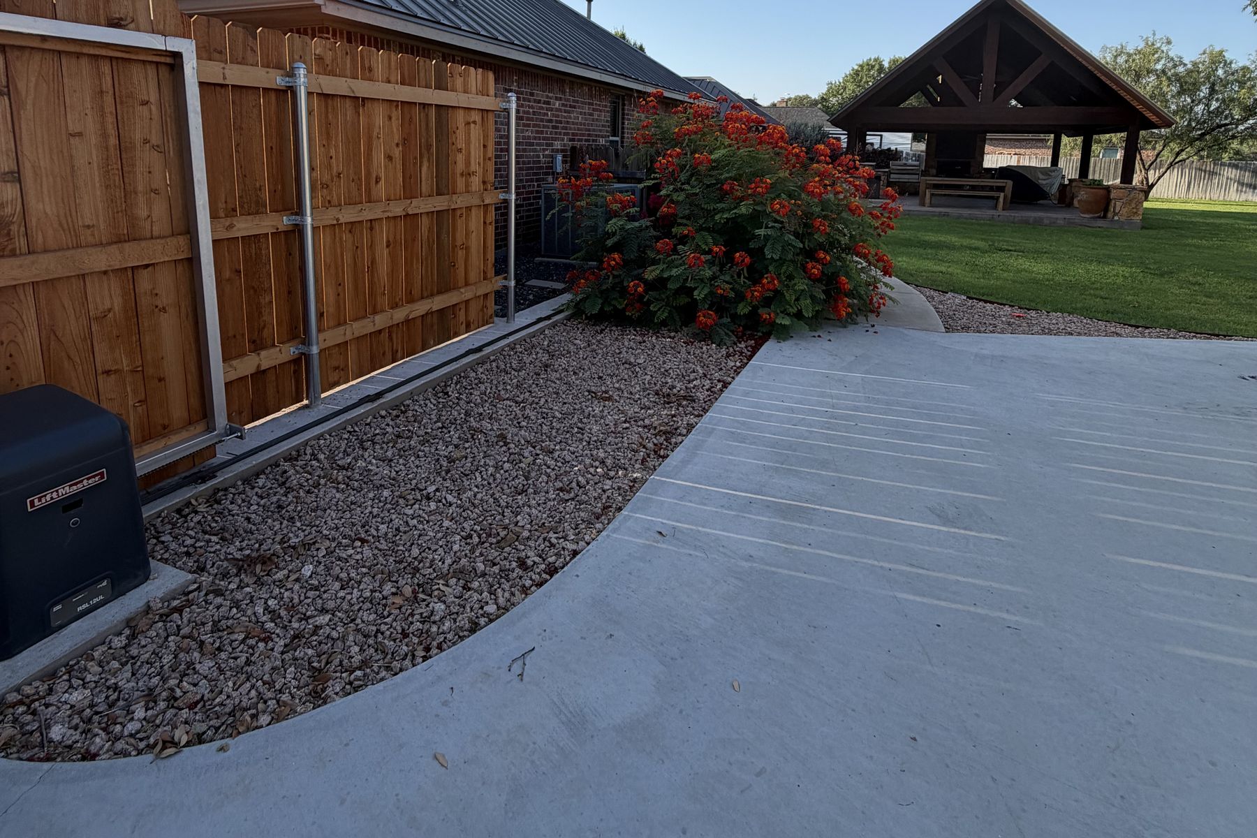 Fence-line bed finished with decorative rock beside a driveway
