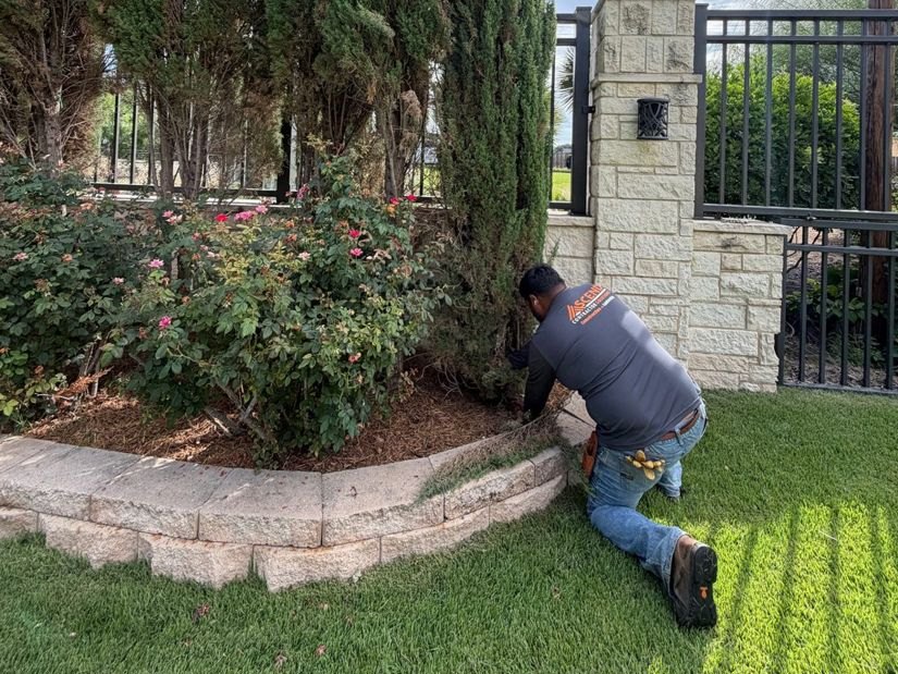 An Ascend crew member finishing a fresh mulch bed along a block retaining wall