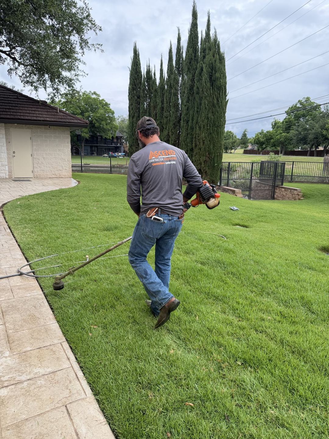 Ascend crew member string-trimming a backyard lawn